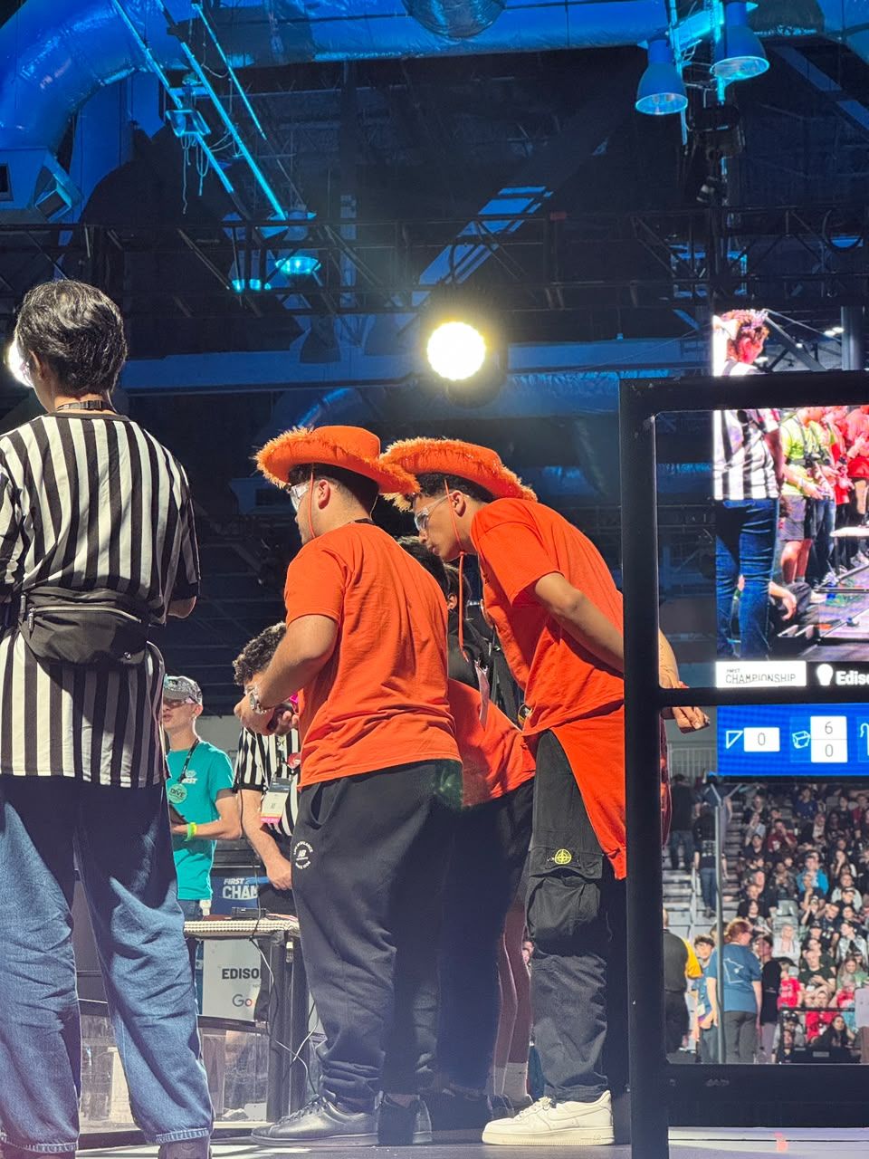 Two drive team members in orange hats lean over the field wall at the FIRST Championship.